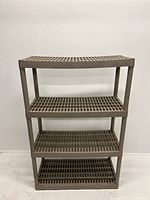 Front view of a brown plastic portable 4-tier shelf unit with grid shelves against a white wall.
