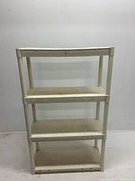 Front view of the white plastic portable shelf unit with four shelves showing the structural details and condition.