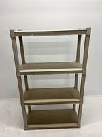 Front view of the beige plastic shelving unit with four shelves, showing overall structure and condition.
