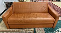 Front view of tan leather sleeper sofa showing seat cushion, backrest, and armrests.