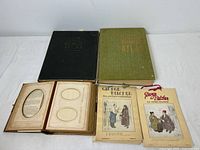 Two vintage world atlas books, two George Belcher picture calendars from the 1930s, and a vintage photo album with ornate cover and multiple photo slots on a white surface.