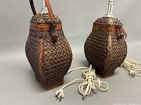 Photo showing both woven rattan lamps side by side, pluggable white cords visible in front.