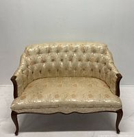 Front view of vintage Regency style upholstered settee with cream and gold floral fabric and carved wood frame.