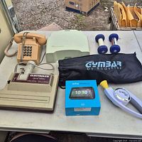 Full lot on table: Electrolux nozzle, two phones, Echo Show box, Bop It, Gymbar bag, dumbbells