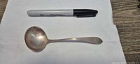 Top view of sterling silver ladle beside marker for scale