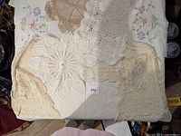 Top-down view of five vintage linens including embroidered tablecloths and crochet doilies spread on flat surface