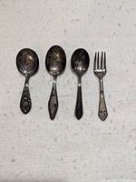 Full view of three baby spoons and one baby fork laid out showing overall condition and decorative details.