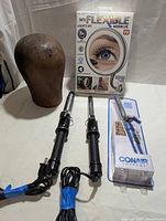 View showing all items: antique wooden wig stand, two curling irons with spiral handles, Conair curling iron in original packaging, and boxed NuBrilliance My Flexible Mirror.
