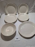 Off-white Corelleware dinner set showing two stacks of round plates, larger oval serving platter and two bowls on white textured background.