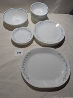 Set of Corelleware with blue flower and leaf pattern: two large serving bowls, one large platter, several small 7-inch plates, large 10-inch plates, and medium bowls.