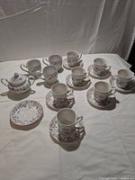 Photo of 7 cups placed on matching saucers, 3 mugs, 9 saucers, and sugar bowl with lid arranged on a white cloth.