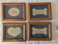 Four framed dog sayings arranged in a horizontal line on a white surface, showing each quote clearly in wooden frames.