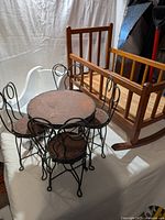 Photo showing doll wooden rocking bed, doll wooden sleigh bed, and round wrought iron doll table with four wrought iron chairs.