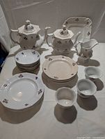 Full set of Chelsea Tea Leaf pattern china displayed on table showing two white octagonal teapots with lids, small pitcher, handleless cups, small bowls, plates, and platter, all decorated with copper luster leaf motifs. Pieces show some discoloration but no chips or cracks.