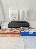 Photo showing Food Saver vacuum sealer with vacuum bags and sealing rolls, mandolin slicer box, and food ricer box arranged neatly on white background