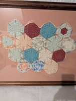 Close-up image showing detail of the crochet hexagon motifs and fabric texture within wooden frame.