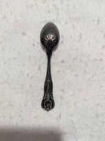 Front view of the ornate decorative spoon showing floral and scrollwork embossed handle and tarnished oval bowl.