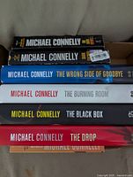 Stack of six Michael Connelly hardcover books showing titles on spine including 'The Burning Room', 'The Black Box', 'The Drop', 'The Wrong Side of Goodbye' and two others.
