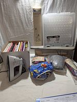 Overall display of the lot including fabric bundles, plastic organizer, travel iron, rolled pattern, and boxed books.
