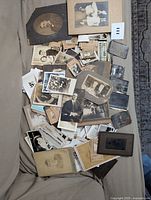 Overview photo showing a large assortment of old photographs in various formats, including tintypes, sepia portraits, and black & white images, some mounted on cardboard and others loose.
