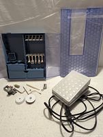 Overview of sewing machine parts laid out: presser feet in case, two bobbins, small parts, foot pedal with cord, and case cover