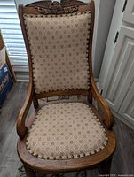 Front view of the wooden rocking chair showing carved eagle top and patterned upholstered seat and backrest