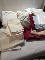 Top-down view of a pile of assorted bedsheets and pillowcases in various colors including cream, white, red, light blue, beige, and light grey.