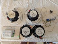 Top view of four Symphony speaker components, amplifier unit, and wiring laid out on white fabric.