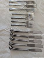 Set of 3 dinner forks and 5 butter knives laid out on cloth