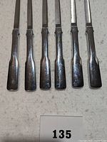 Six stainless steel steak knives laid out in a row showing the handles.