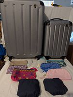 Front view of two gray hard-sided rolling suitcases with assorted travel bags arranged in front.