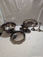 Wide view showing all six plated items on a neutral backdrop including two bowls, a gravy boat with drip tray, two candle sticks, and an oval bread tray.