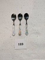 Front view of three vintage spoons showing floral decorated porcelain handles and polished metal bowls.