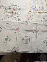 Six pieces of vintage hand-embroidered textiles arranged on a surface showing floral and grid patterns