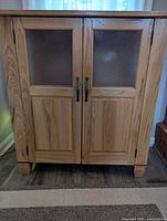 Closed wine cabinet showing wood finish, frosted glass doors, and dark metal handles.