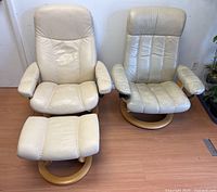 Pair of 1970s Ekornes Stressless Norwegian lounge chairs with cream distressed leather and wooden swivel bases, each accompanied by matching footstool.