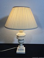 Front view of the lit alabaster table lamp with pleated fabric shade showing the overall design and lamp in working condition.