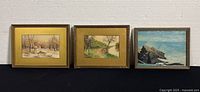 Photo of three small framed oil paintings showing winter, summer, and rocky seaside scenes