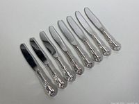 Eight dessert knives arranged in a row, clear view of ornate sterling silver handles and polished stainless steel blades.