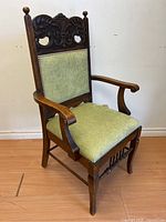 Front diagonal view of the antique wooden armchair showing carved scroll back, armrests, and upholstered seat and backrest.