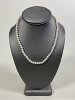 Front view of the 17 inch pearl necklace displayed on a black bust showing round white pearls evenly spaced.