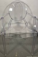 Front view of transparent Louis Kartell style ghost chair showing oval back, armrests, and seat.