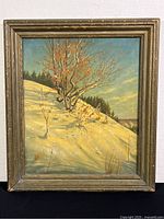 Full view of the framed painting showing winter landscape with tree on a snowy hillside under a blue sky.