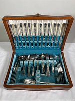 Full view of open wooden case showing entire flatware set inside with knives in the lid and various forks, spoons and serving utensils in the main compartment.