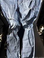 Full view of one pair of blue distressed Buffalo jeans showing waistband, zipper area and distressed fabric.