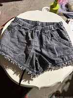 Black jean shorts with elastic waistband and frayed hem shown on table