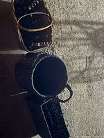 Three baskets placed on a rough surface. The black rectangular basket, round black basket with handles, and brown wooden basket with handles are shown from varying angles.