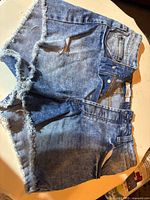 Front side view of two pairs of denim jean shorts showing frayed hems and pockets