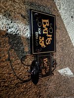 Photo showing the bathroom wall sign and soap holder placed on concrete surface, highlighting the vintage style of the items with clear text on the sign and the metal soap holder shape.