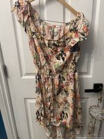 Full view of Adrene floral dress on a hanger showing the colorful floral pattern and ruffled neckline.
